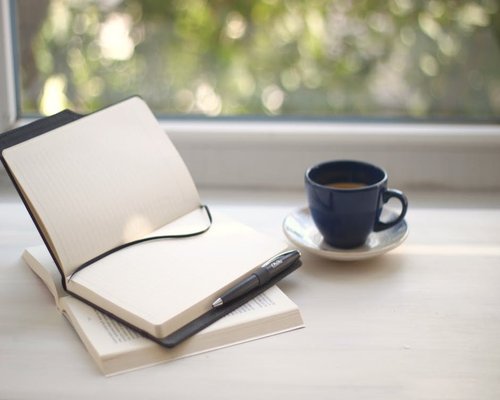 Minimalist home desk near a bright window with a cup of coffee and notebook